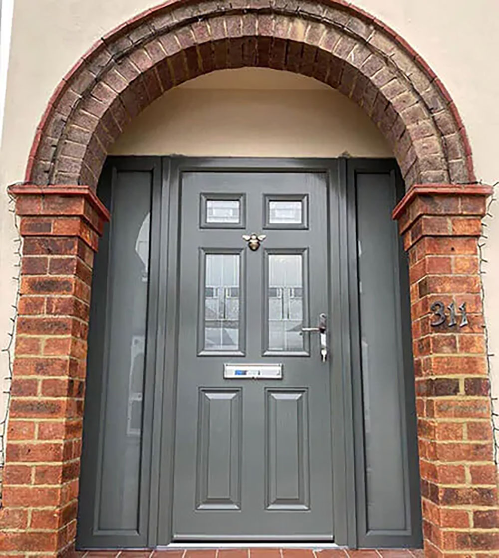 Traditional grey composite door with side panel, set in a wide red brick archway with glazed inserts and traditional panel moulding